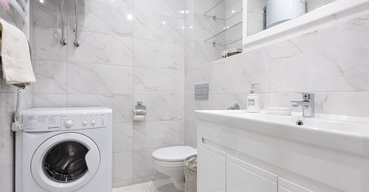 Lavadora blanca instalada en un baño de mármol claro, junto al inodoro y un lavabo moderno.