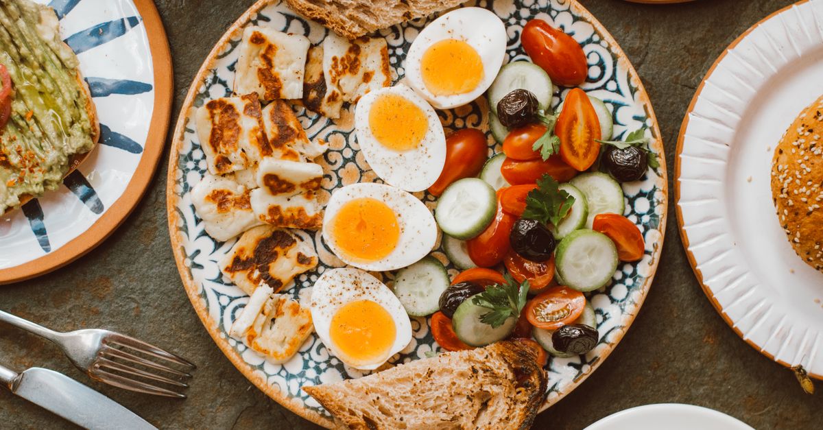 Plato con huevos cocidos partidos por la mitad, yema líquida, tomates cherry, pepino y pan tostado alrededor.