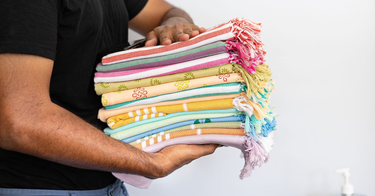 Una persona sostiene una pila de toallas finas de colores variados dobladas prolijamente.