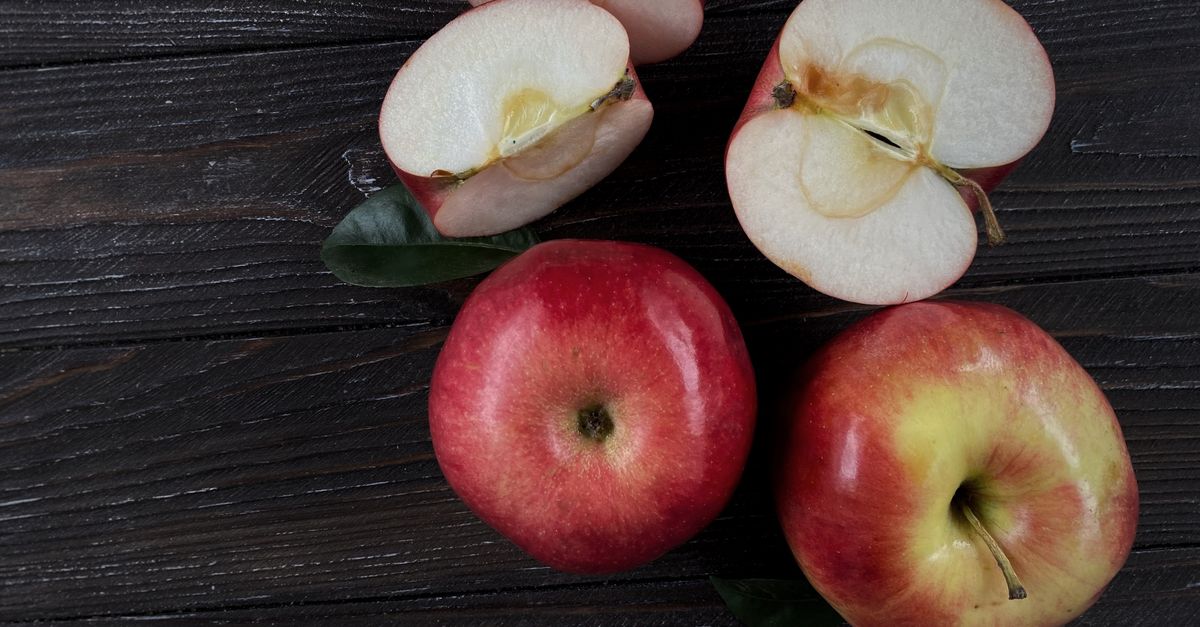Manzanas rojas enteras y cortadas por la mitad sobre una superficie de madera oscura, mostrando su pulpa fresca.