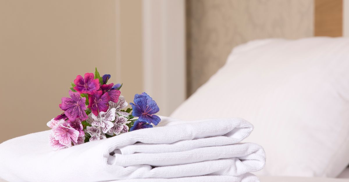 Un ramo de flores moradas y blancas colocado sobre un juego de toallas blancas dobladas en una cama.