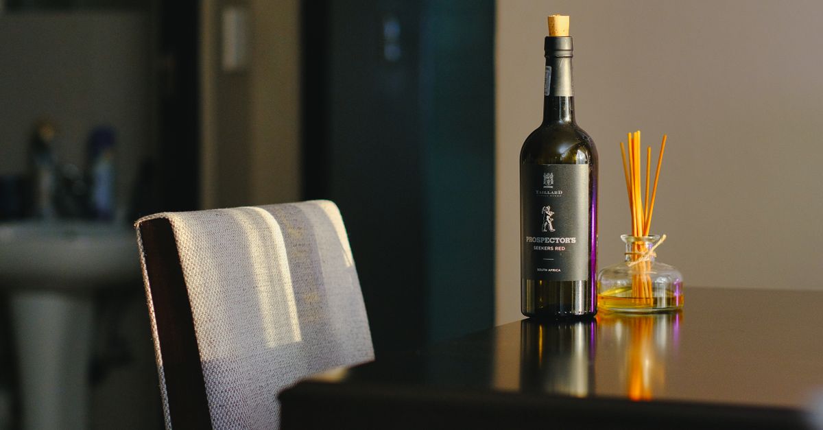 Una botella de vino tinto con el corcho puesto sobre una mesa de madera oscura, junto a un difusor de aromas.
