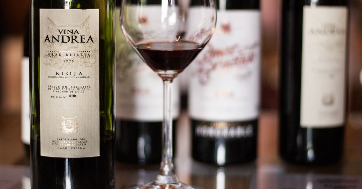 Una copa con vino tinto servido junto a botellas de vino Rioja con etiquetas visibles sobre una mesa.