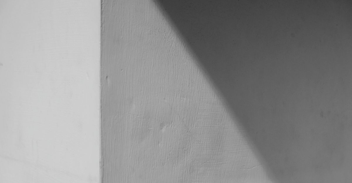 Esquina de una pared con textura visible y una sombra diagonal que sugiere ligeras variaciones de tono en la superficie.