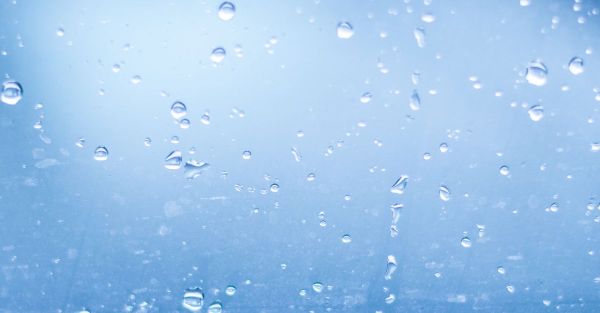 Cristal de ventana cubierto de gotas de agua con luz natural iluminando el fondo azulado.