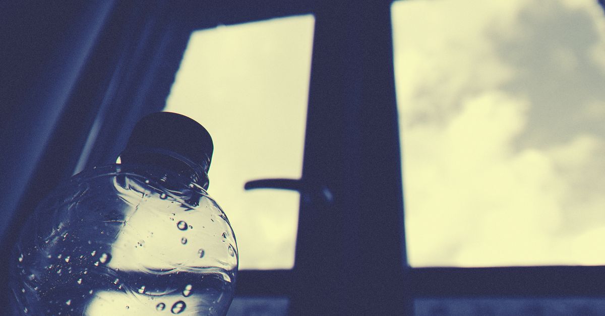 Ventana con vidrio transparente y una botella de agua en primer plano, con el cielo visible al fondo.