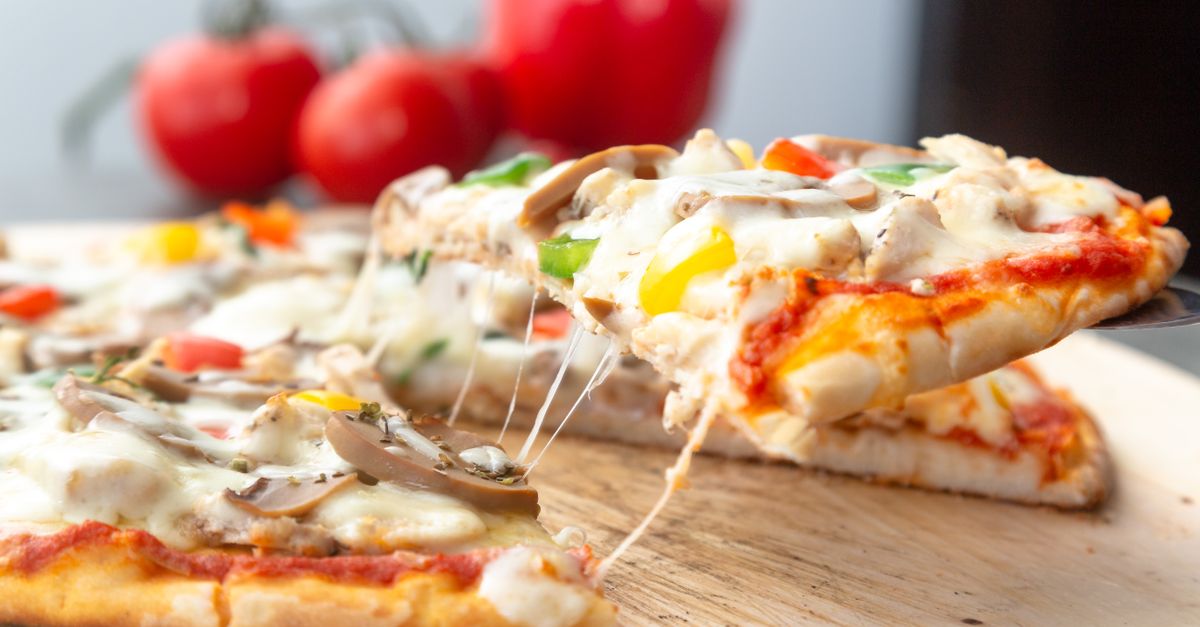 Una porción de pizza con queso fundido, champiñones y pimientos se levanta con una espátula, mostrando hilos de queso derretido.