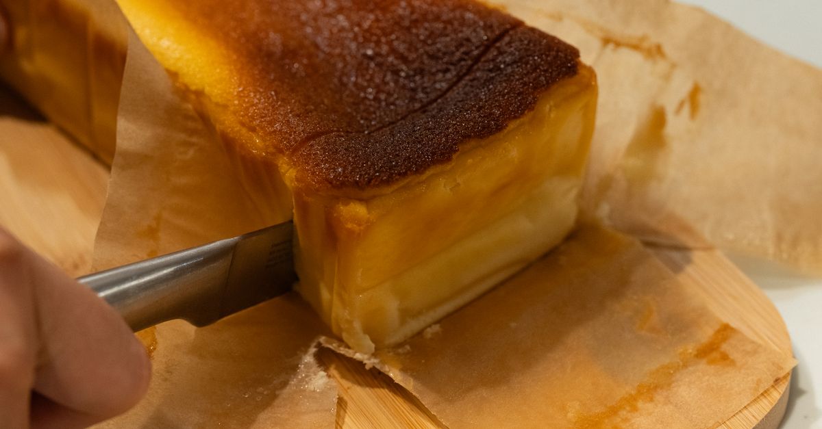 Un bloque de queso envuelto en papel, cortado con un cuchillo sobre una tabla de madera.