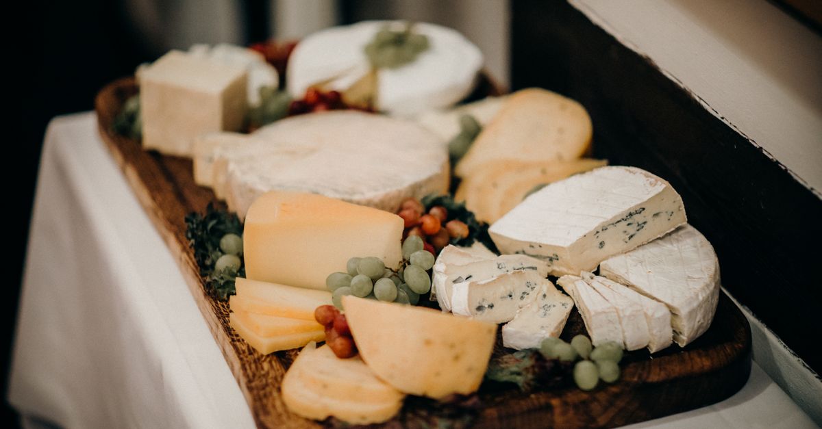 Una tabla de madera con una variedad de quesos curados y blandos, incluyendo cuñas y trozos de queso azul, acompañados de uvas.