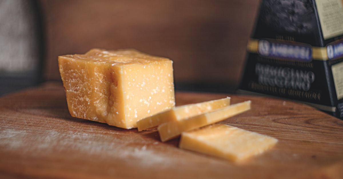Un trozo de queso parmesano cortado sobre una tabla de madera, con lonchas finas junto a él y su envoltorio en el fondo.