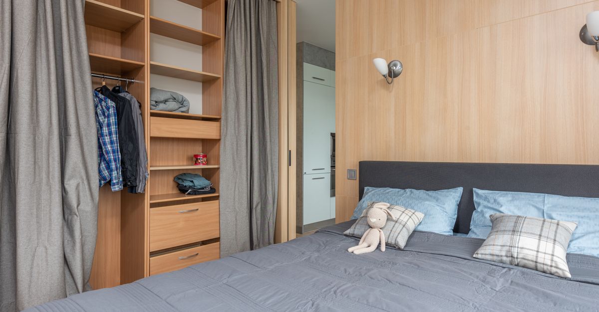 Dormitorio con armario abierto ordenado con pocas prendas y una cama con almohadas junto a él.