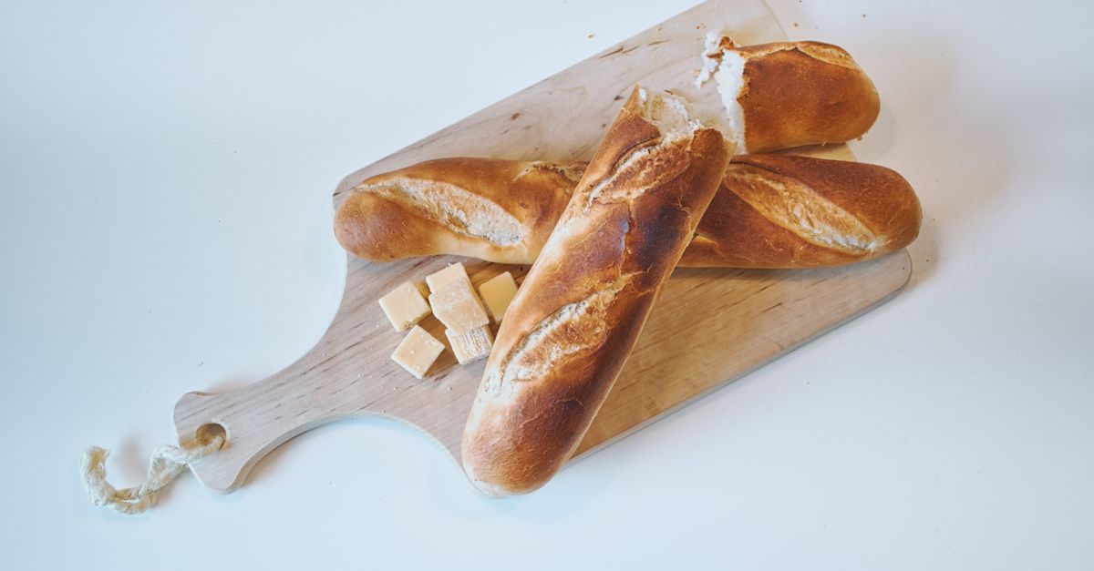 Varias barras de pan sobre una tabla de madera, con pequeños cubos de pan cortados junto a ellas.