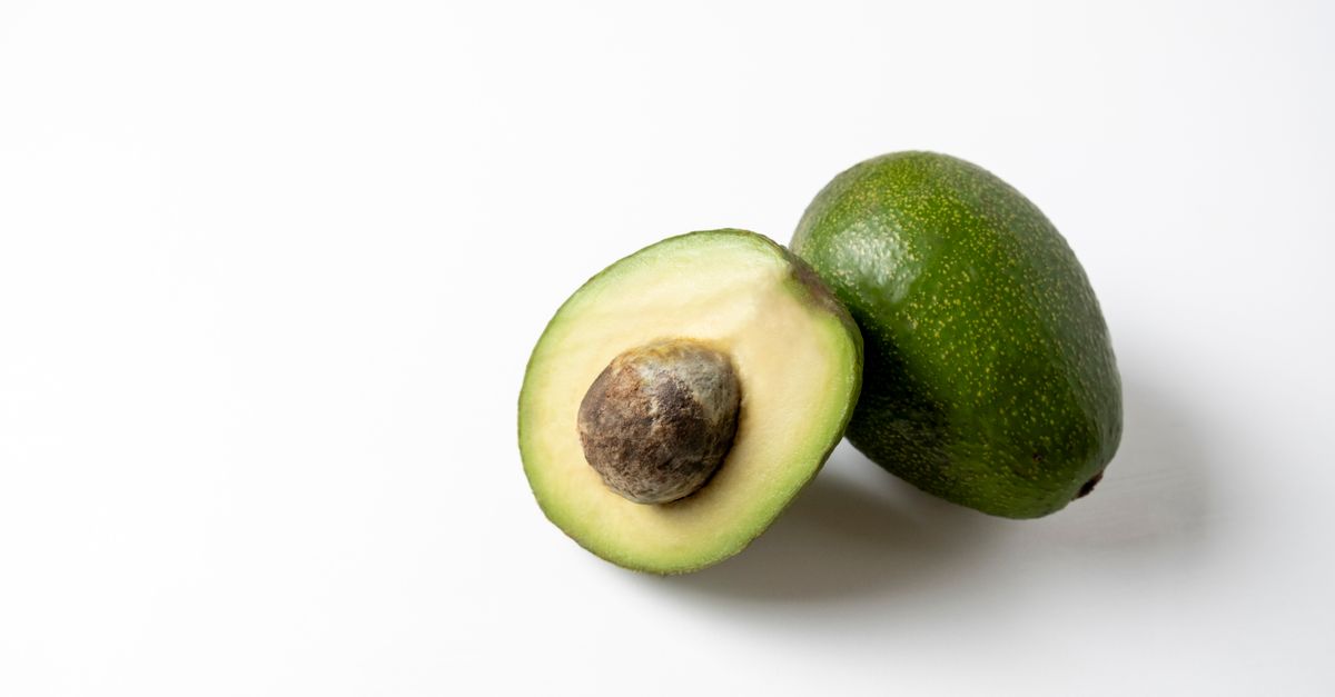 Un aguacate cortado por la mitad junto a otro entero, mostrando la pulpa verde y el hueso, sobre fondo blanco.