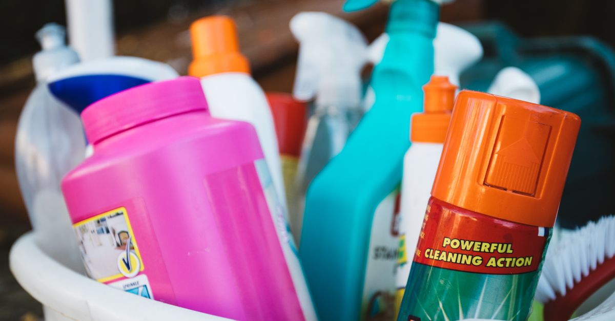 Un cesto lleno de botellas y aerosoles de productos de limpieza de colores variados, incluyendo uno con la etiqueta 'Powerful Cleaning Action'.