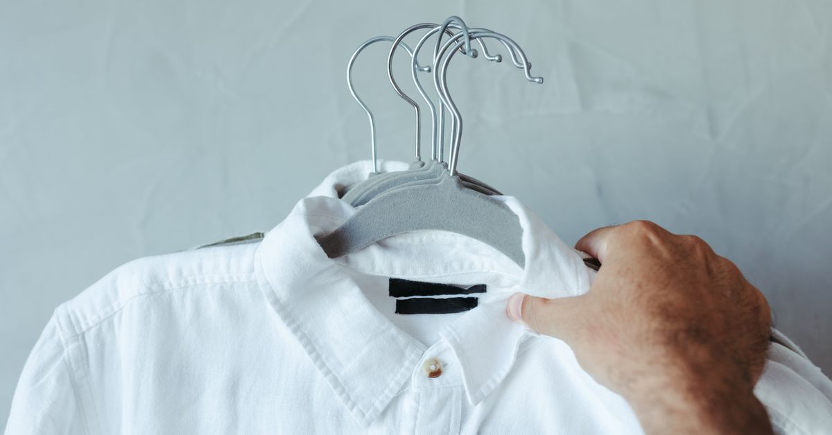 Una persona sostiene el cuello de una camisa blanca colgada, examinando de cerca el tejido en busca de manchas.
