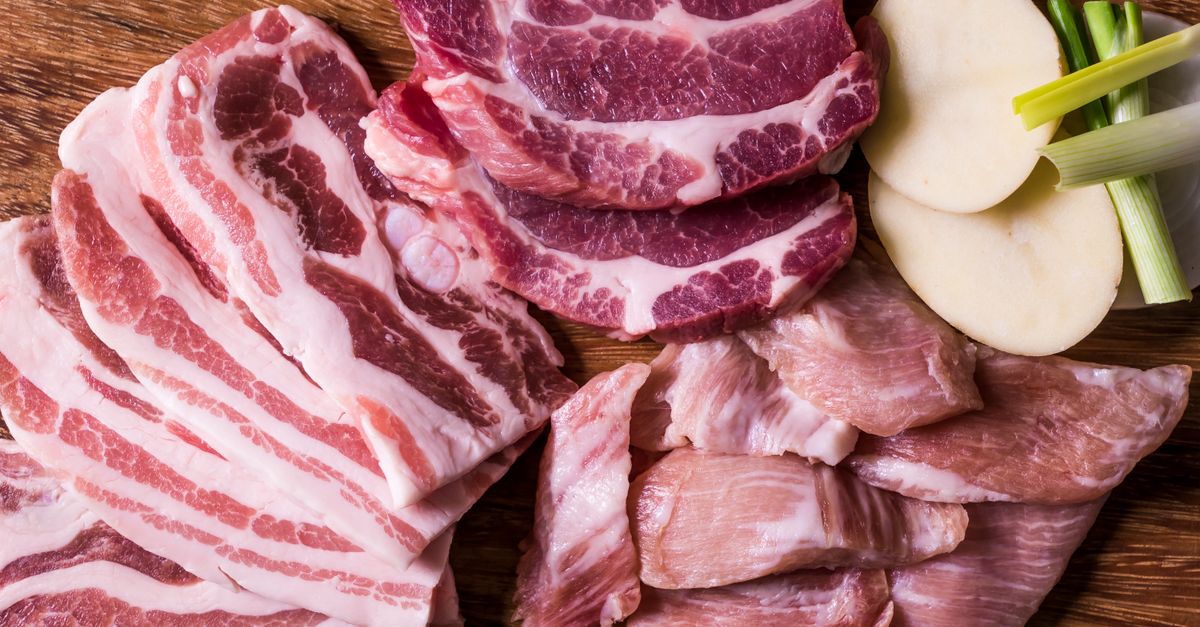 Vista cenital de distintos cortes de carne cruda en finas lonchas sobre una tabla de madera, junto a rodajas de patata y cebolleta.