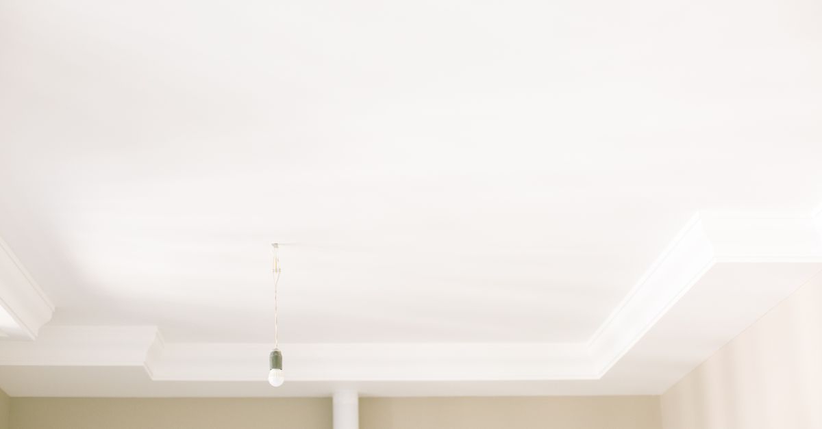 Rincón de un techo blanco con moldura decorativa y una bombilla colgante, sin ventilación visible ni señales de humedad.