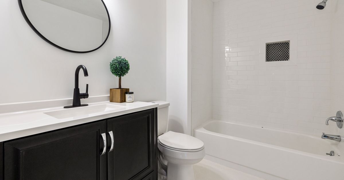 Cuarto de baño con bañera blanca empotrada, alicatado de azulejos tipo metro blanco y mueble de lavabo oscuro con encimera blanca.