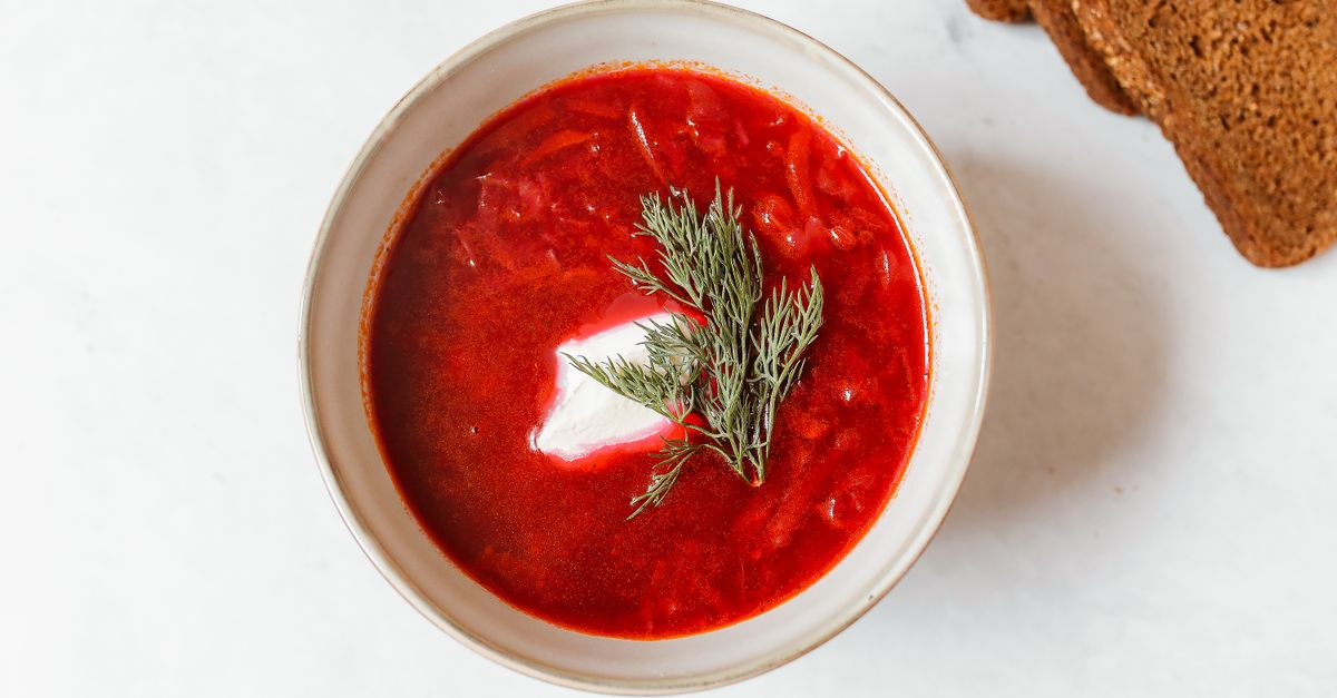 Cuenco de sopa roja (borsch) con un toque de nata agria y eneldo fresco, servido junto a pan negro.