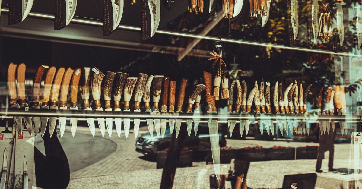 Vitrina de una tienda con una amplia selección de cuchillos de cocina colgados en fila, con mangos de madera y asta.