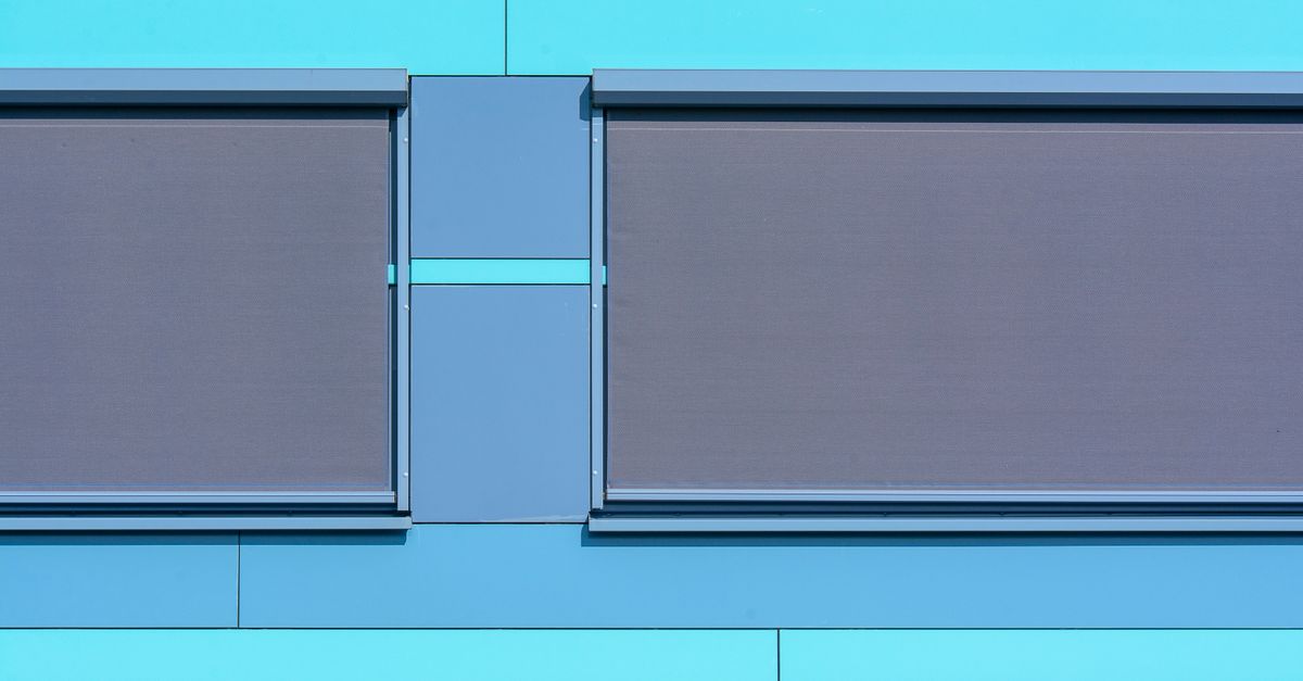 Persianas enrollables de aluminio gris instaladas en el exterior de una fachada azul turquesa.