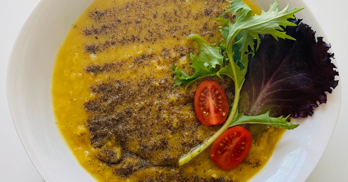 Un plato blanco con un guiso cremoso de lentejas amarillas espolvoreado con especias y decorado con hojas de ensalada y tomates cherry.