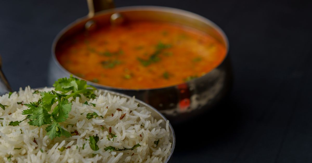 Un cazo metálico con un guiso de lentejas naranjas con cilantro, junto a un plato de arroz basmati con hierbas.